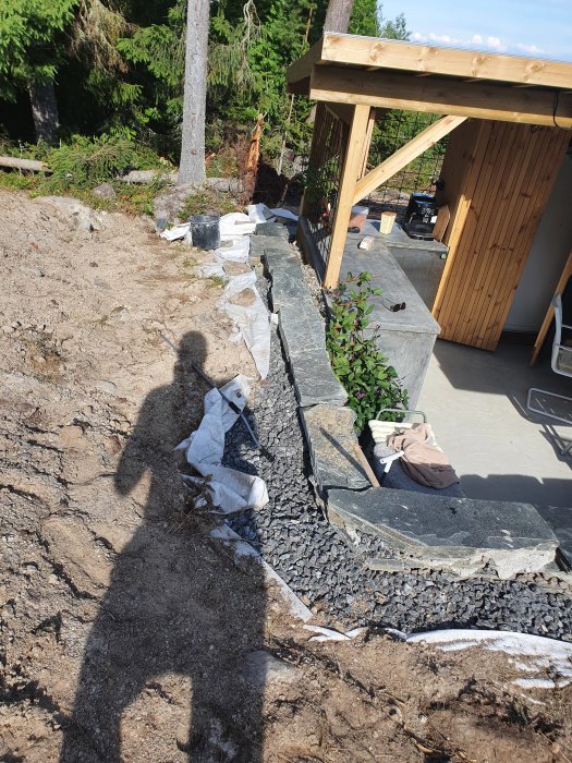 Nybyggd stenmur med grus och markduk vid en byggarbetsplats, väntande på plantering.