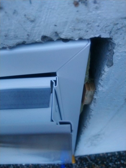 Närbild av en dörrkarm som tar emot mot en betongvägg med synlig betongskruv och träkil.