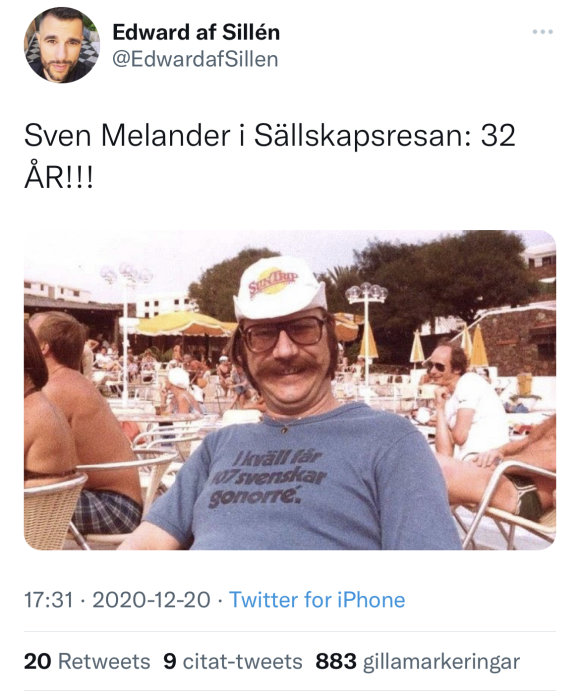 Man i solhatt och t-shirt sitter med ett leende framför poolområde fullt med människor.