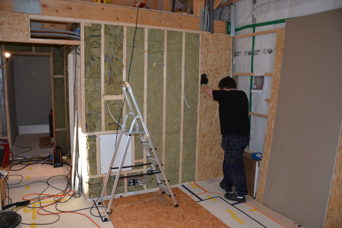 Person monterar OSB-skivor på stommen i ett under konstruktion rum med isolering synlig.