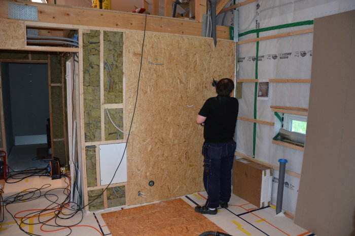 En person som installerar OSB-panel på en isolerad vägg i en renoveringsprocess.