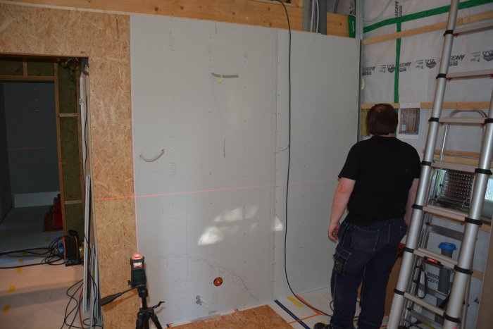 Person i arbetskläder monterar gipsvägg med hjälp av laserpass i ett pågående renoveringsprojekt