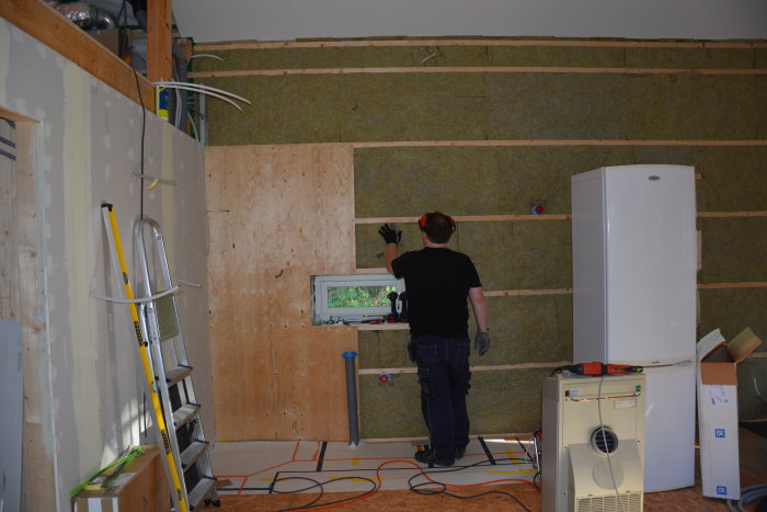 Person monterar isolering och reglar för väggbeklädnad i ett under-renovering rum.