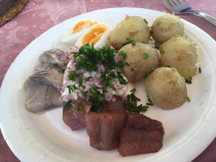 Tallrik med sommarmat bestående av kokta potatisar, sill, hackad rödlök, gräslök och ett halvt ägg.