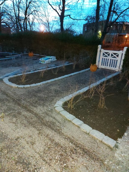 Trädgård med smågatsten och ny kantlinje av storgatsten, tomma säckar och bar vegetation.