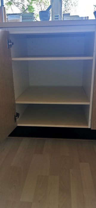 Öppet köksskåp inför installation av diskmaskin, med hyllplan och synlig skruv i bakkant.