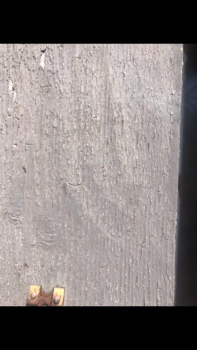 Sliten träyta med befintlig grå färg som flagar och visar tecken på slitage, med en rostig metallfäste i förgrunden.