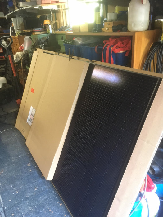 Solpanel ligger mot kartong i ett rörigt garage, väntar på installation.