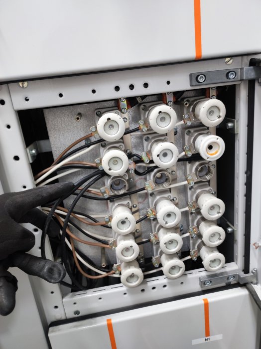 Elutrustning med flera kopplade keramikhållare och elektriska kablar i ett elskåp.