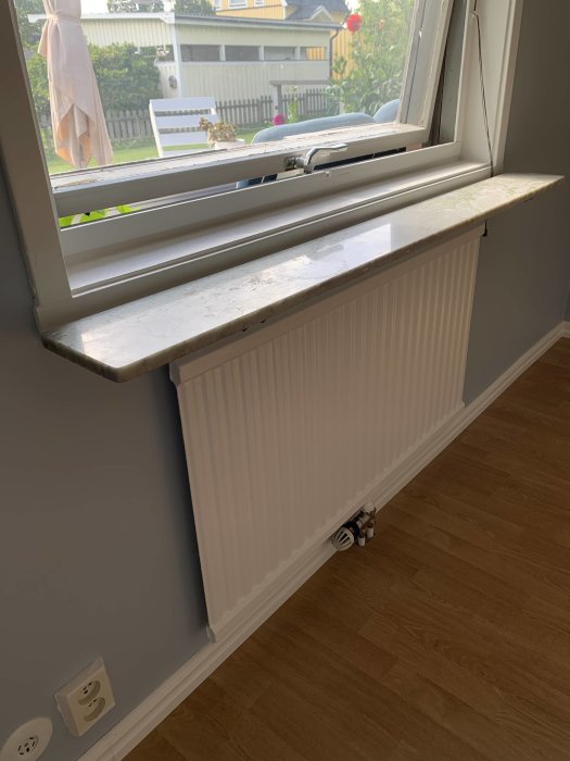 Nyligen renoverat rum med nymålade väggar och radiator under ett fönster, med detaljer som ska slutföras.