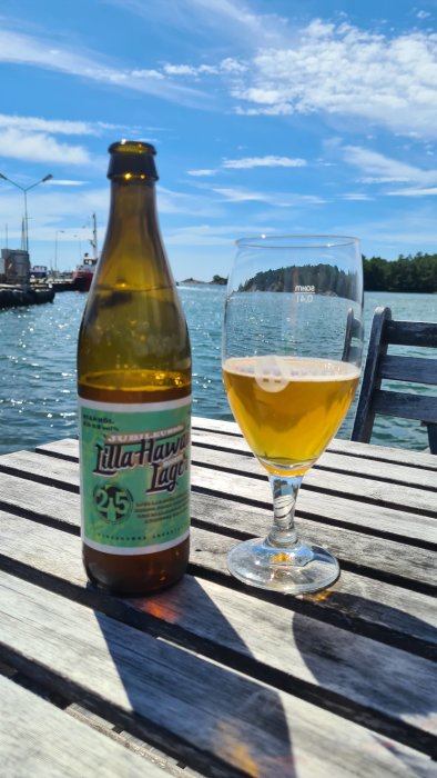 Ölflaska och glas på ett bord vid havet, med firande av Nynäshamns Ångbryggeris 25-årsjubileum.