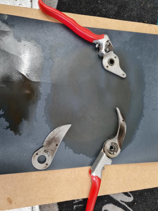 Nedmonterade trädgårdssaxar med röda handtag på en grå yta, redo för slipning.