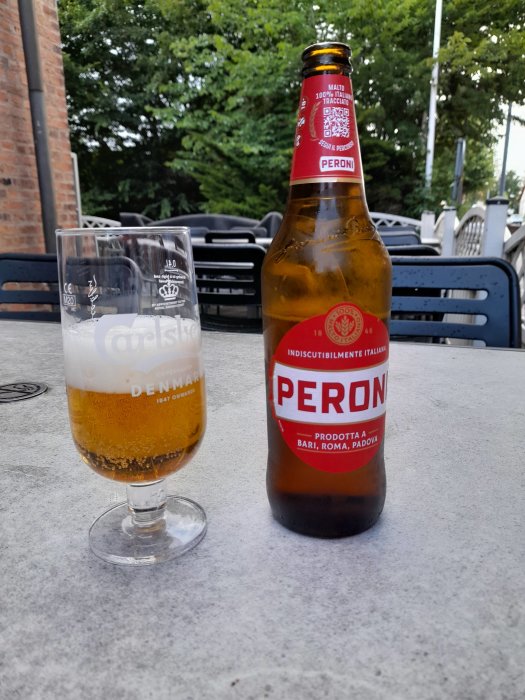 En flaska Peroni öl bredvid ett halvfullt glas på ett utomhusbord.