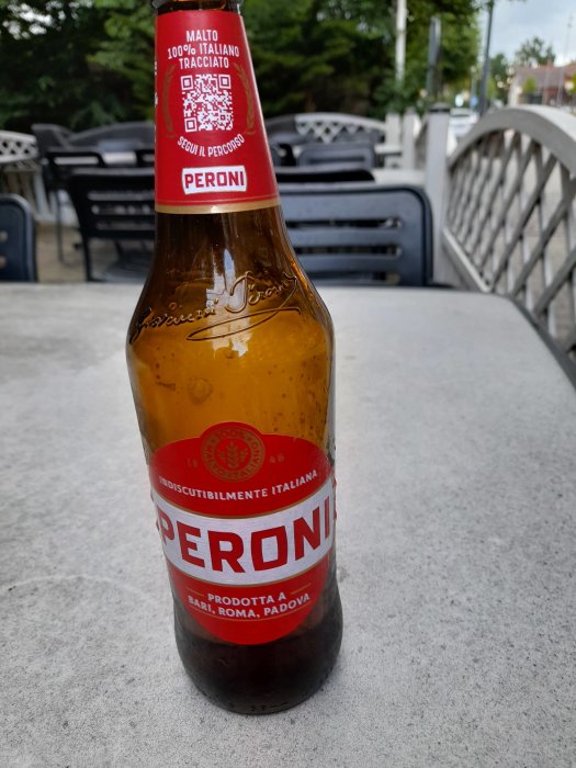 En flaska Peroni öl på ett bord med suddig uteservering i bakgrunden.