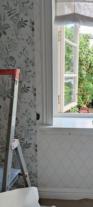 Ny tapet med blommönster vid ett fönster och en stege, oavslutad tapetsering vid en vägguttag.
