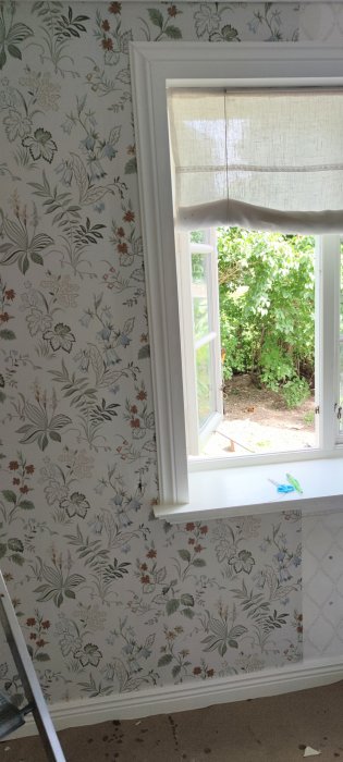 Nyligen tapetserat sovrum med blommigt mönster runt ett fönster, sax på fönsterbrädan, blick mot trädgården.