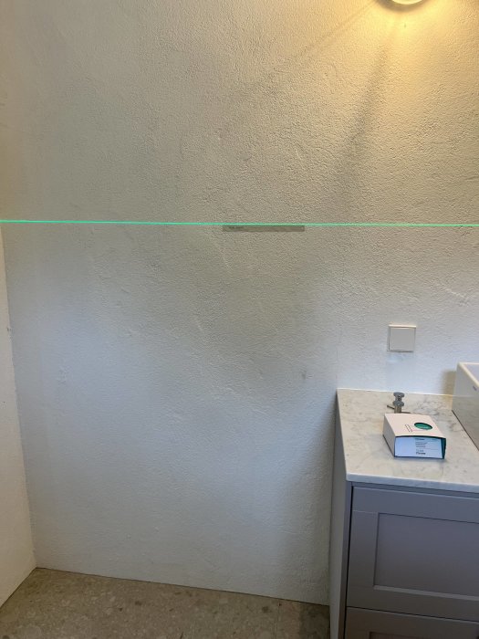 En halvfärdig tvättstuga med gråa väggar, grön maskeringstejp och grått skåp med marmorliknande topp.