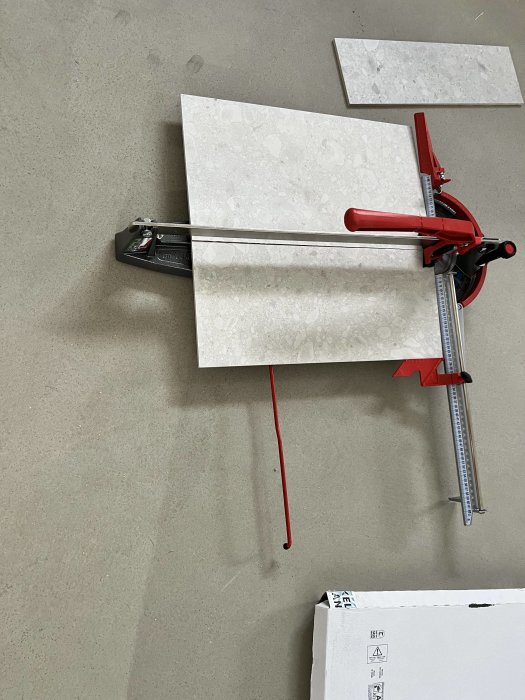 Kakelplattor som skärs med en kakelskärare på en betonggolv.