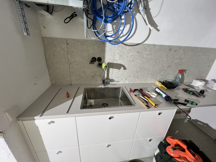 Tvättstuga under renovering med handfat och diverse verktyg utspridda på bänkskivan.