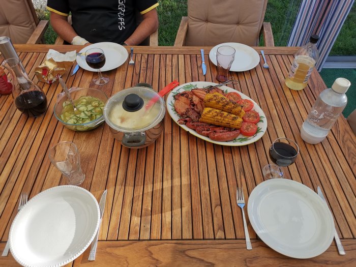 Grillad kassler med glaze, majskolvar, gurksallad och potatismos serverat på utomhusbord.