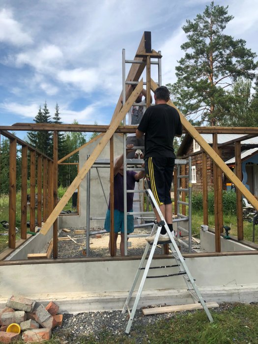 Två personer monterar upp en nockbalk på en stomme av trä på ett byggprojekt.