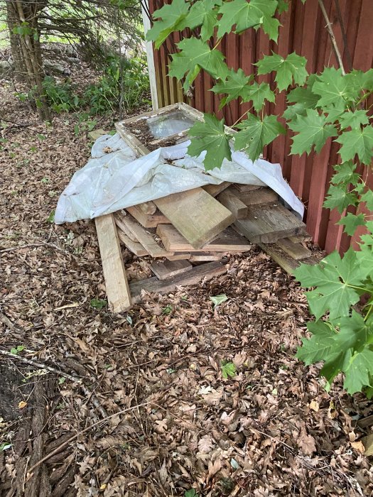 En hög med diverse gamla prylar och byggavfall som ligger utslängt vid ett hus i naturen.