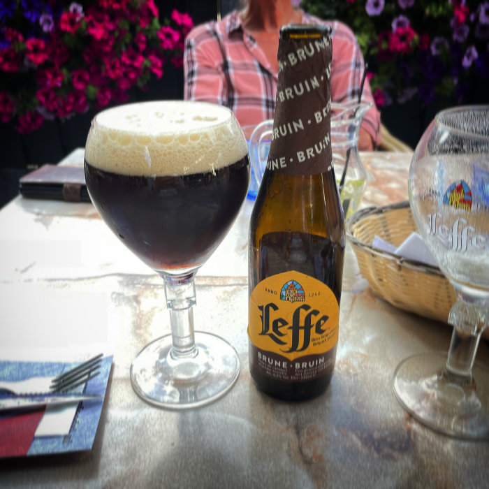 Ett glas mörkt öl framför en öppen flaska av Leffe Brune på ett bord med suddig bakgrund.