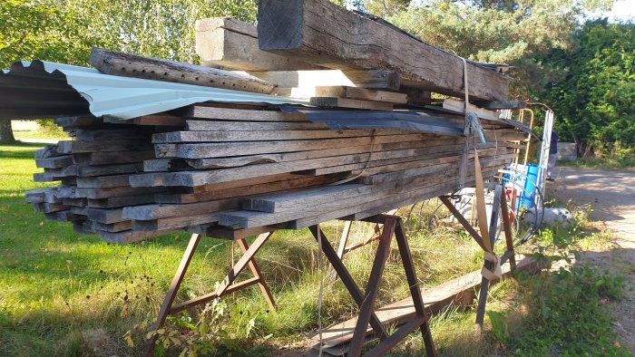 Stapel av åldrade ekplankor under takplåtar utomhus, några stockar ovanpå, lagrade i 25 år.