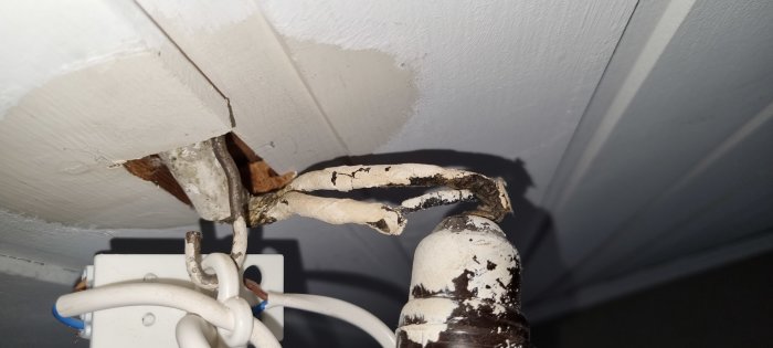 Äldre sliten elinstallation med uppluckrat isoleringsmaterial vid en takbelysningsanslutning i ett hus från 50-talet.