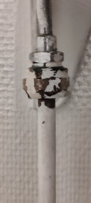 Flagnande vit färg på ett rör och koppling mot en vägg.