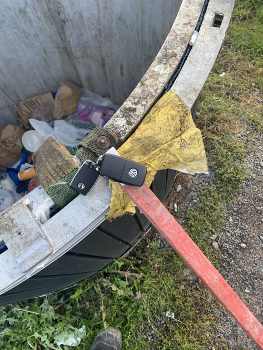 Bilnyckel fästad vid ände av spett med dubbelhäftande tejp, räddad från djup soptunna.