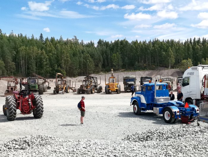 Besökare på traktor och maskinträff med olika fordon som traktorer och en lastbil framför skogsområde.