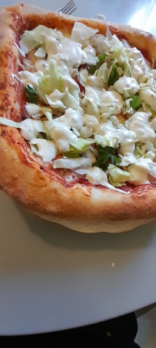 Pizza med sallad och vit sås på en vit tallrik.