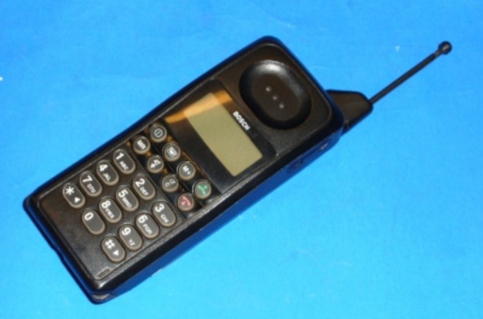 En gammal Bosch mobiltelefon från 1996 med utdragbar antenn och numeriskt tangentbord på blå bakgrund.