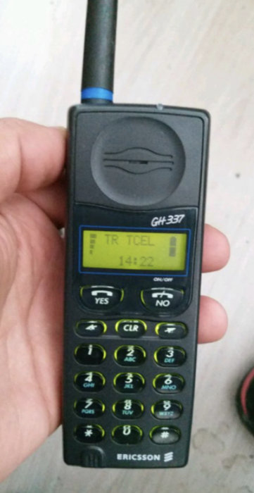 En hand som håller en Ericsson GH 337 mobiltelefon med utskjuten antenn och displayen visar klockslaget 14:22.