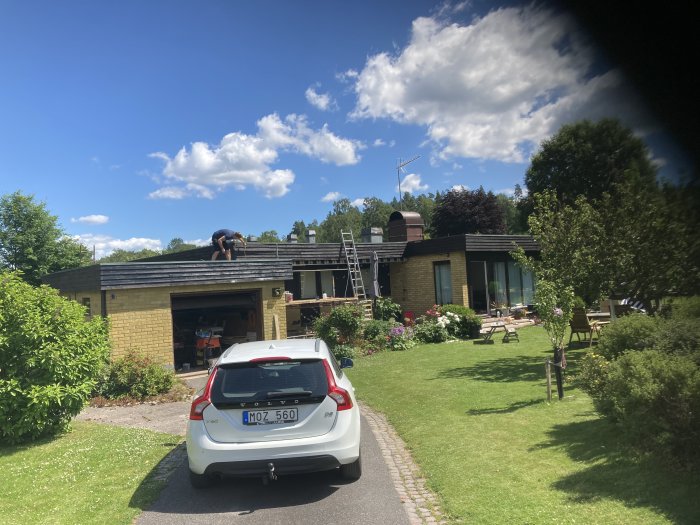 Gult mexitegelhus med svartmålade träpartier och garageport, med trädgård och en person på taket.