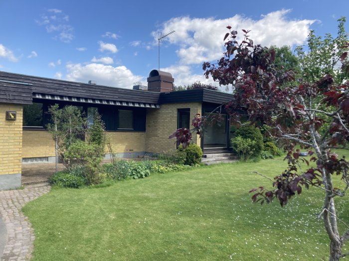 Gult mexitegelhus med svarta träpartier, grönskande trädgård och blå himmel.