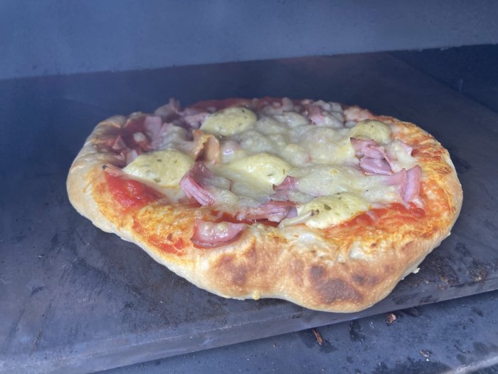 Nybakad pizza med skinka och ananas i pizzaugn.