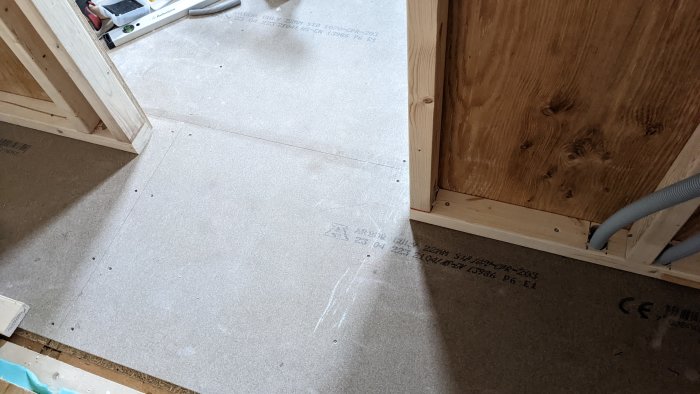 Oförberett golv i byggfas redo för flytspackling med synliga golvspånskivor och en obehandlad trätröskel.