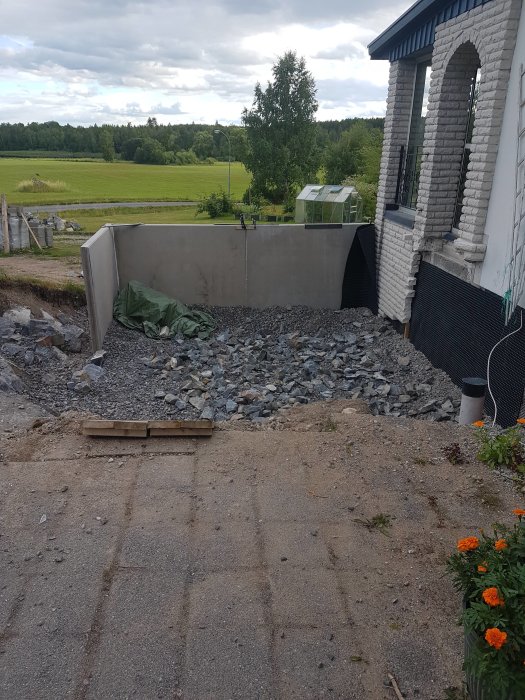 Återfyllning av grus nära nyinstallerade L-stöd vid ett hus med utsikt över ett fält.