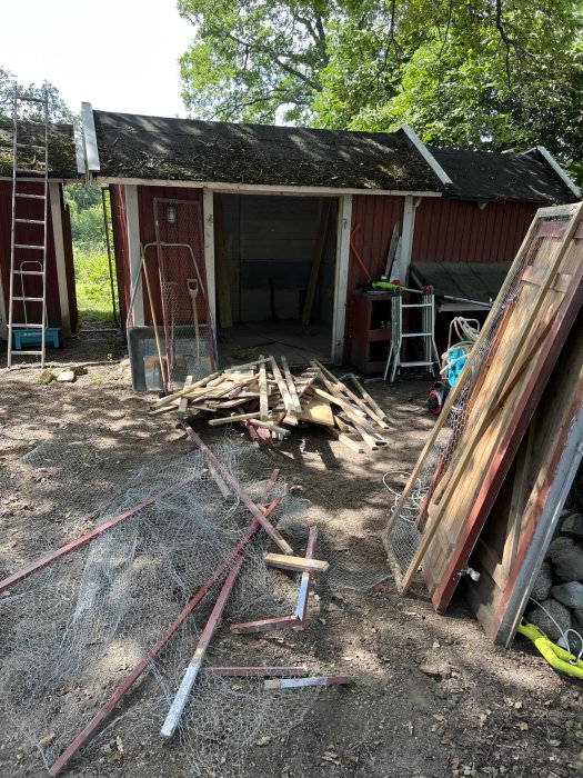 Röd träbyggnad under renovering med avlägsnat tak och spillvirke utspritt framför, bredvid en stege och högtryckstvätt.