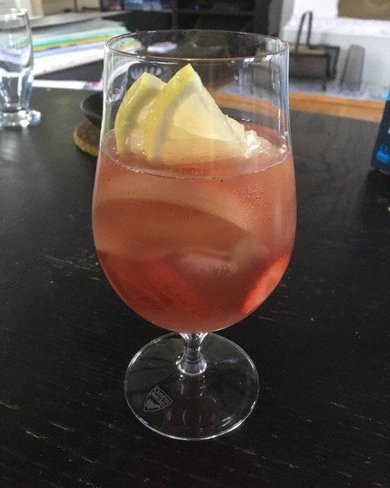 Ett glas rabarbersangria med is och citronskivor på ett mörkt bord.