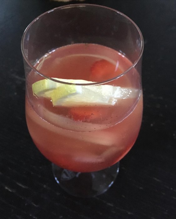Ett glas fyllt med rabarbersangria och isbitar på ett mörkt bord.
