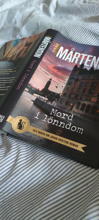 Bok med titeln "MORD i lönnådom" på en randig bädd.