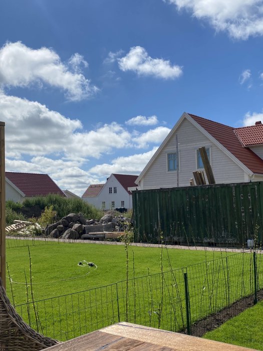 Grannens röriga trädgård med stora stenar, en grön container och trädgårdsavfall, sedd från en altan.