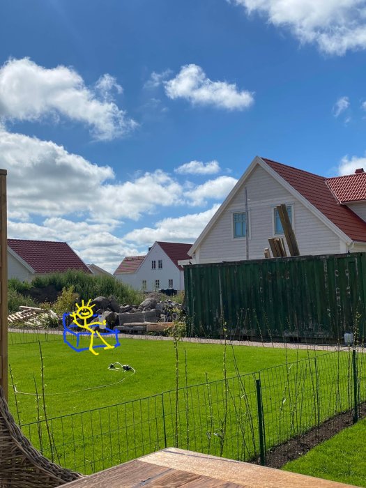 En solstol på en välhållen gräsmatta med ett tecknat gult och blått solkarakter som sitter på stolen framför hus och klarblå himmel.