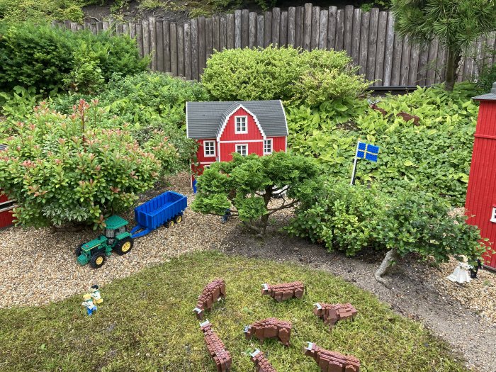Miniatyrmodell av en bondgård med röda byggnader, grön traktor, blå vagn, leksaksfigurer och svensk flagga.