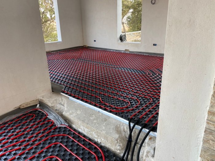 Installation av golvvärme med röd värmeslinga på svart stödplatta på en betonggolvkonstruktion.