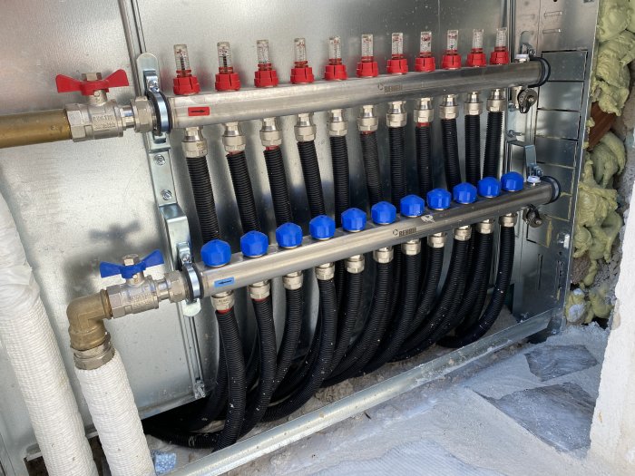 Fördelare för värmesystem med många anslutna svarta rör och blå och röda ventiler i ett byggprojekt.