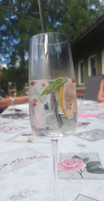 Vin- eller drinkglas fyllt med dryck, citronskiva och bär, på ett bord utomhus.